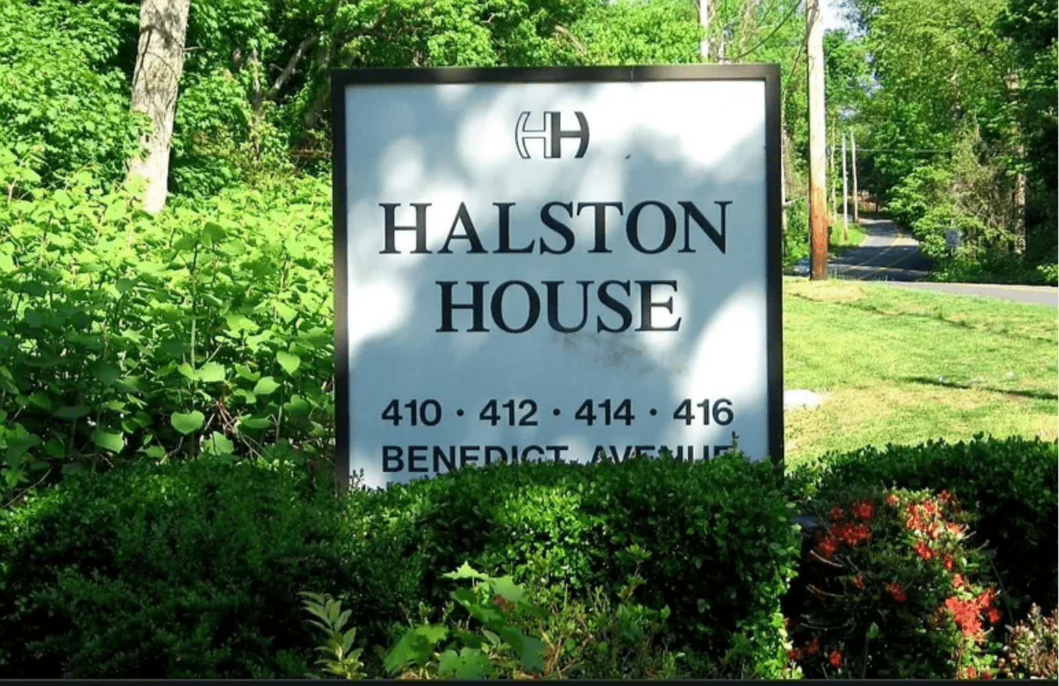 Sign for Halston House with apartment numbers in a leafy setting.